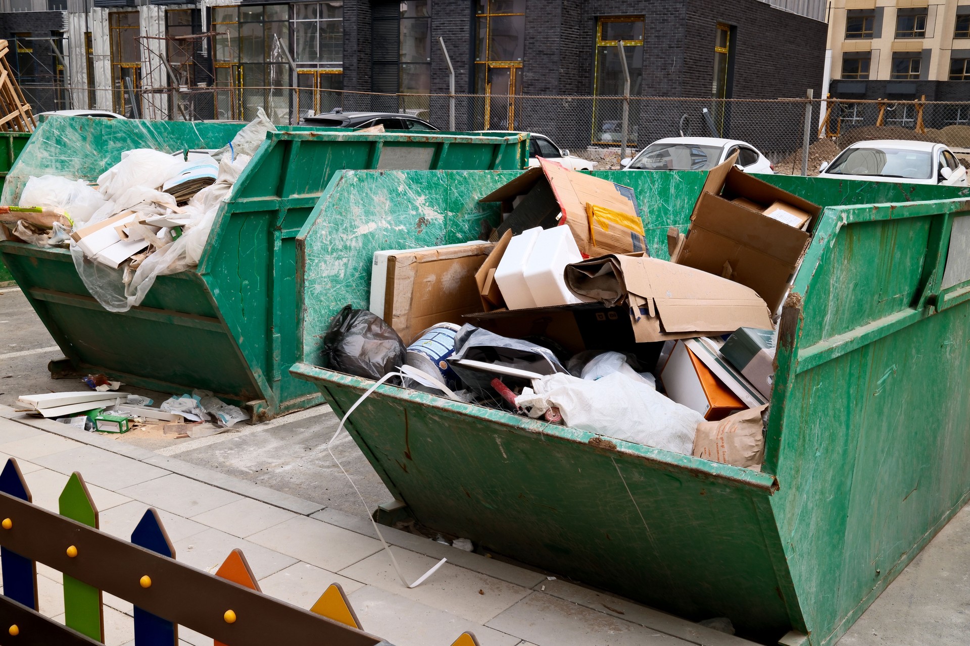 Overflowing green construction dumpster filled with cardboard boxes and building waste at urban construction site Overflowing green construction dumpster filled with cardboard boxes and building waste at urban construction site